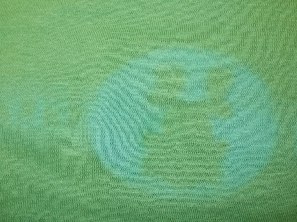 A ghost image on the back of a shirt, mirroring the white ink print on the shirt under it in the stack.